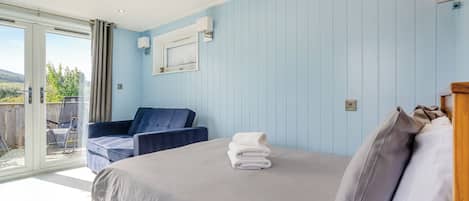 Ein Schlafzimmer mit Bett, Stuhl, Fenster und Blick ins Freie.