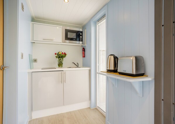 A compact kitchen with white cabinets, a microwave, a toaster, and a vase with flowers on the counter. - 1 bedroom accommodation in Great Busby (Great Busby)