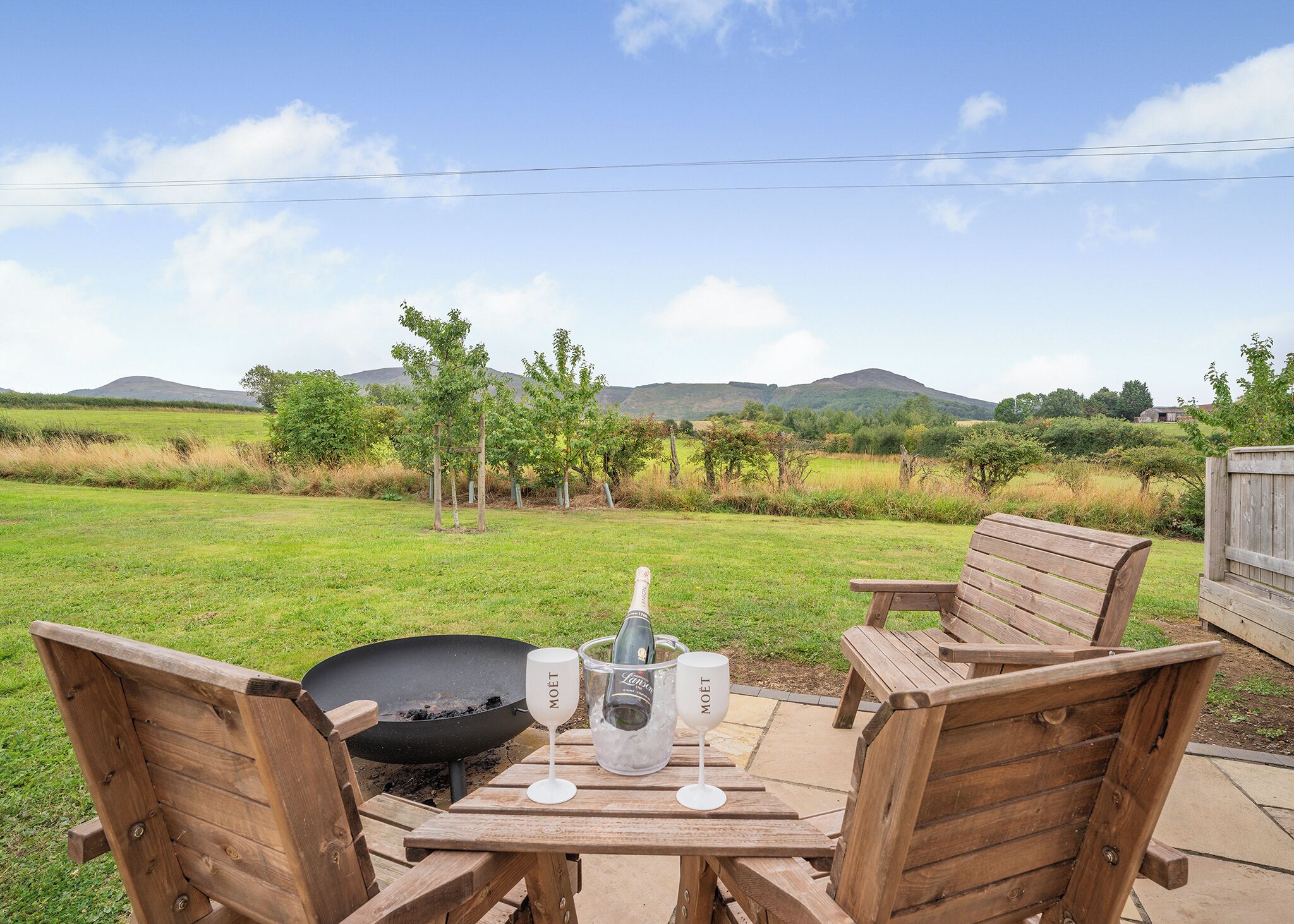 An outdoor patio with wooden furniture, a grill, and a wine glass labeled 'MOET' on a table.