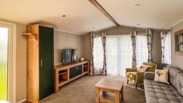 Una sala de estar con sofá, mesa de centro, televisor sobre un mueble de madera y ventana con cortinas.