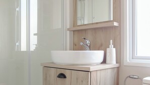 Un baño con un lavabo blanco, un espejo encima y una ventana a la derecha.