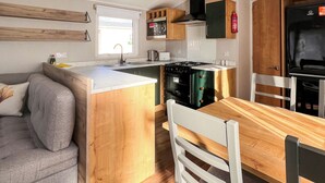 Una cocina compacta con armarios de madera, una isla central, una mesa de comedor con sillas y un horno empotrado.