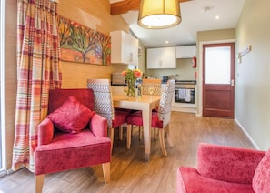 Een moderne woonkamer met rode fluweelstoelen, een houten eettafel en een keuken op de achtergrond.