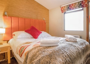 Een hotelkamer met een houten hoofdbord, een bed met witte beddengoed en een rode kussen, een zacht tapijt en een raam met gordijnen.