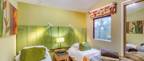 A room with two beds, a nightstand, a lamp, a window with curtains, and a mirror.