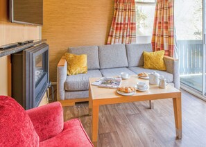 A living room with a grey sofa, yellow pillows, a wooden coffee table with croissants and cups, a television, and a red chair. - Cosy traditional lodge with one double and one twin. (Millom)