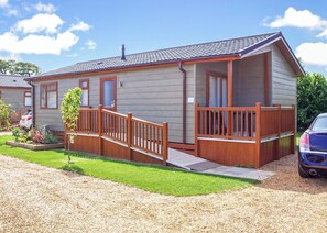A single-story mobile home with a front deck, a small garden area, and a gravel driveway. - 2 bedroom accommodation in Hunstanton (Hunstanton)