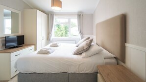 Ein Schlafzimmer mit Bett, Nachttisch, Fernseher und einem Fenster mit Vorhängen.