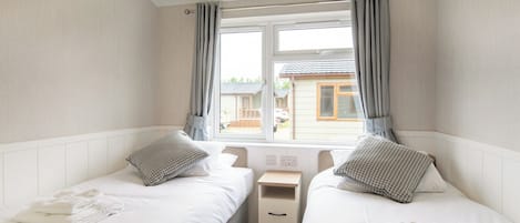 A bedroom with two beds, a window with curtains, a bedside table, and a lamp.
