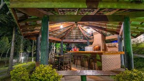 Un espacio al aire libre con asador, horno de ladrillo, mesas de madera y taburetes de bar.