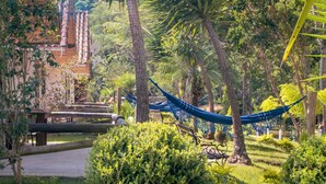 Una hamaca en un jardín exuberante con un puente de madera y un edificio al fondo.
