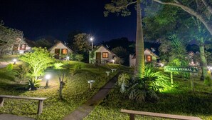 Una vista nocturna de Villa Pinhal con senderos bien iluminados, pequeñas casas y abundante vegetación.