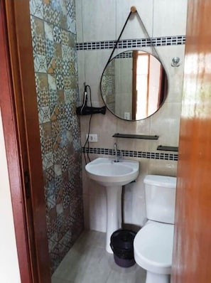 Un baño con pared de azulejos, lavamanos pedestal, inodoro y espejo redondo.
