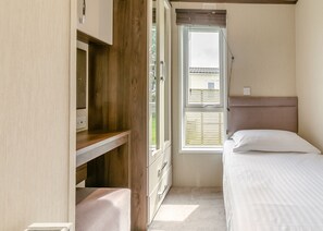 A bedroom with a bed, a wooden desk, a window with blinds, and a view of a house outside.