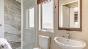 Et badeværelse med brusekabine i glas, toilet, vask og spejl.