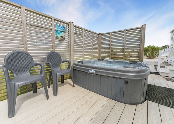 A wooden deck with a hot tub and two plastic chairs.