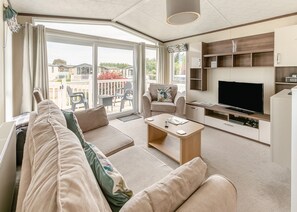 A modern living room with a sofa, armchair, coffee table, TV, and built-in shelving. - Sandy Pebble Deluxe (Pet) (Looe)