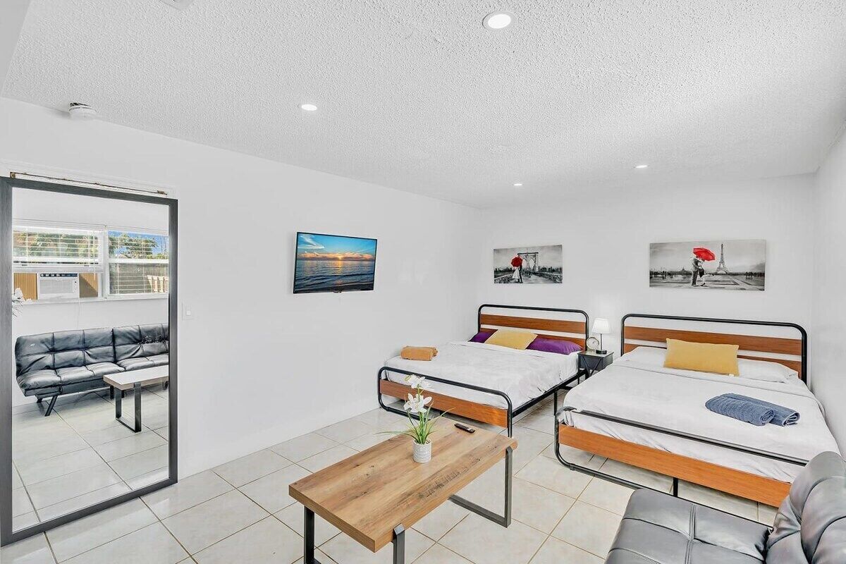 A modern, well-lit room with two beds, a sofa, a coffee table, and a view of the outside.