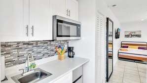 A modern kitchen with white cabinets, a stainless steel sink, and a microwave. There is a coffee maker and utensils on the counter.