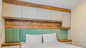 Ein Bett mit hölzernem Kopfteil, gepolstertem, grünen Kopfteil und weißer Bettwäsche.