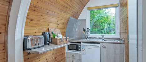 Eine kleine Küche mit Holzwänden, einem Fenster mit Blick und einer Toaster, einem Wasserkocher sowie einer Mikrowelle.