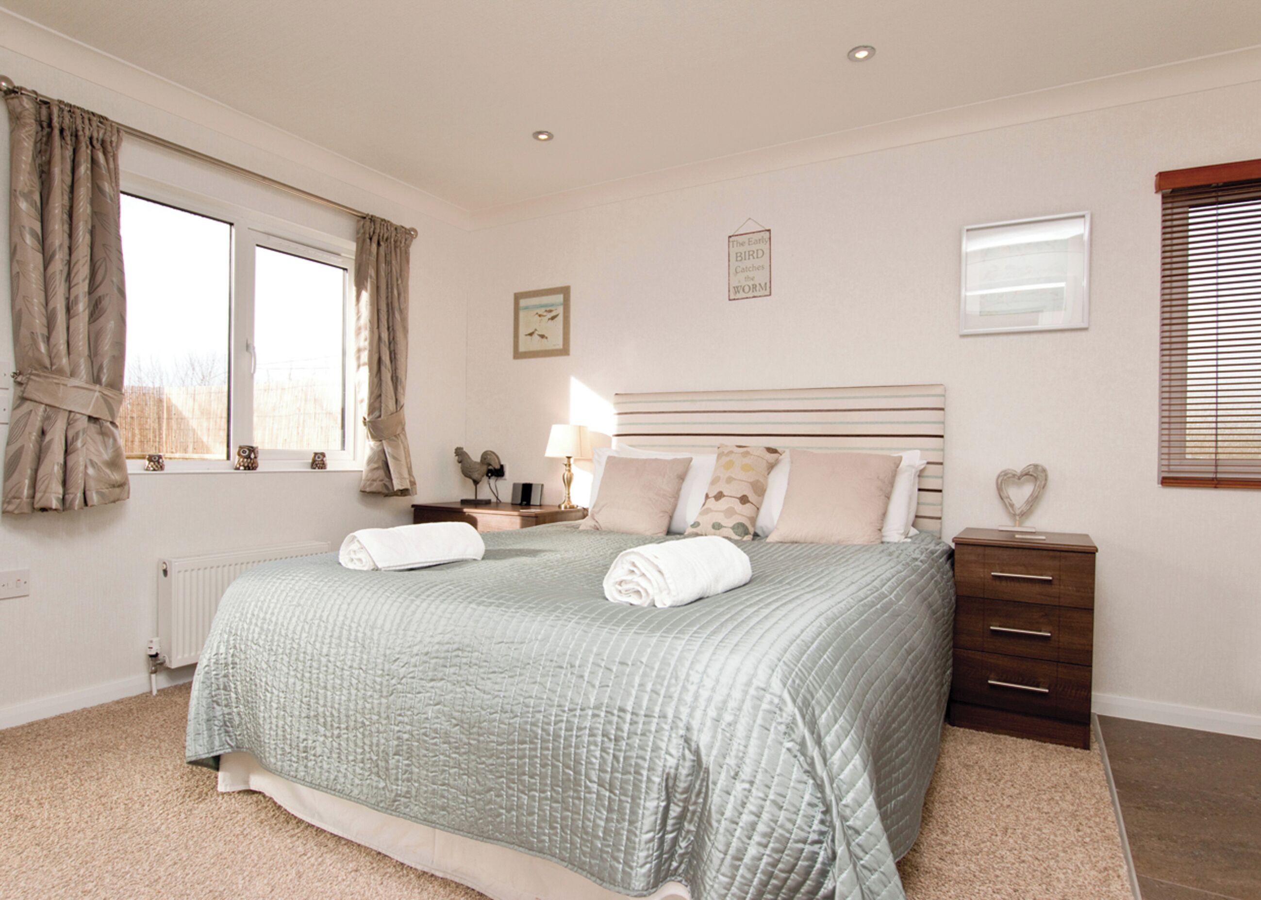 A neatly arranged bedroom with a large bed, bedside tables, a dresser, and a window with curtains.