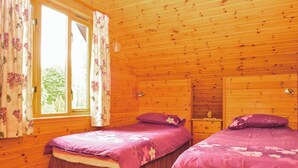 Uma cabana com duas camas de madeira, uma janela com cortinas e um aparador de madeira.