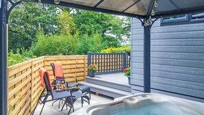 Un bain à remous avec une terrasse en bois, une chaise et une table avec un plateau en verre.