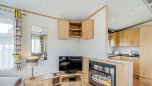 A compact living space with a TV, wooden cabinets, a fireplace, and a kitchen area. - 1 bedroom accommodation in Alyth, Perthshire (Alyth, Perthshire)