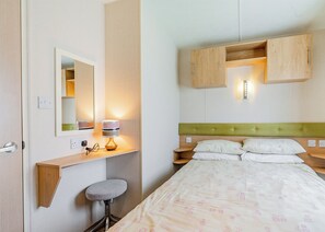 Hotellihuone, jossa on sänky, yöpöytä, lamppu, peili ja pieni jakkara.