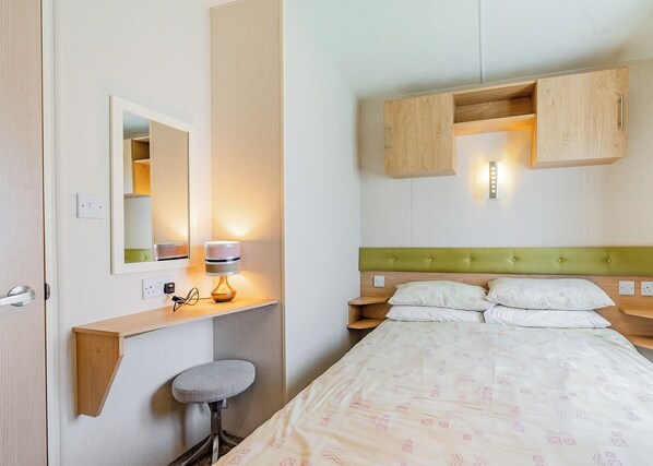 A hotel room with a bed, a bedside table, a lamp, a mirror, and a small stool.