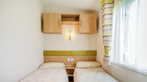 A small room with two beds, wooden headboards, a light fixture above the beds, and a window with curtains. - 1 bedroom accommodation in Alyth, Perthshire (Alyth, Perthshire)