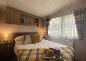 A bedroom with a bed, bedside lamps, a window with curtains, and a tray with breakfast items.
