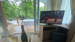Quarto com televisão, uma garrafa de champanhe e duas taças sobre uma mesa.