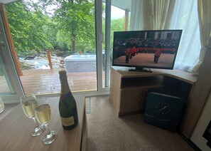 A room with a television, a bottle of champagne, and two glasses on a table. - 2 bedroom accommodation in Snowdonia (Snowdonia)