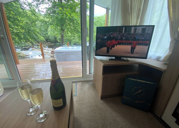 Una habitación con una televisión, una botella de champán y dos copas sobre una mesa.