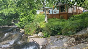 A cabin with a view of a flowing river, surrounded by dense greenery and trees. - 2 bedroom accommodation in Snowdonia (Snowdonia)