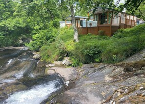 A cabin with a view of a flowing river, surrounded by dense greenery and trees. - 2 bedroom accommodation in Snowdonia (Snowdonia)