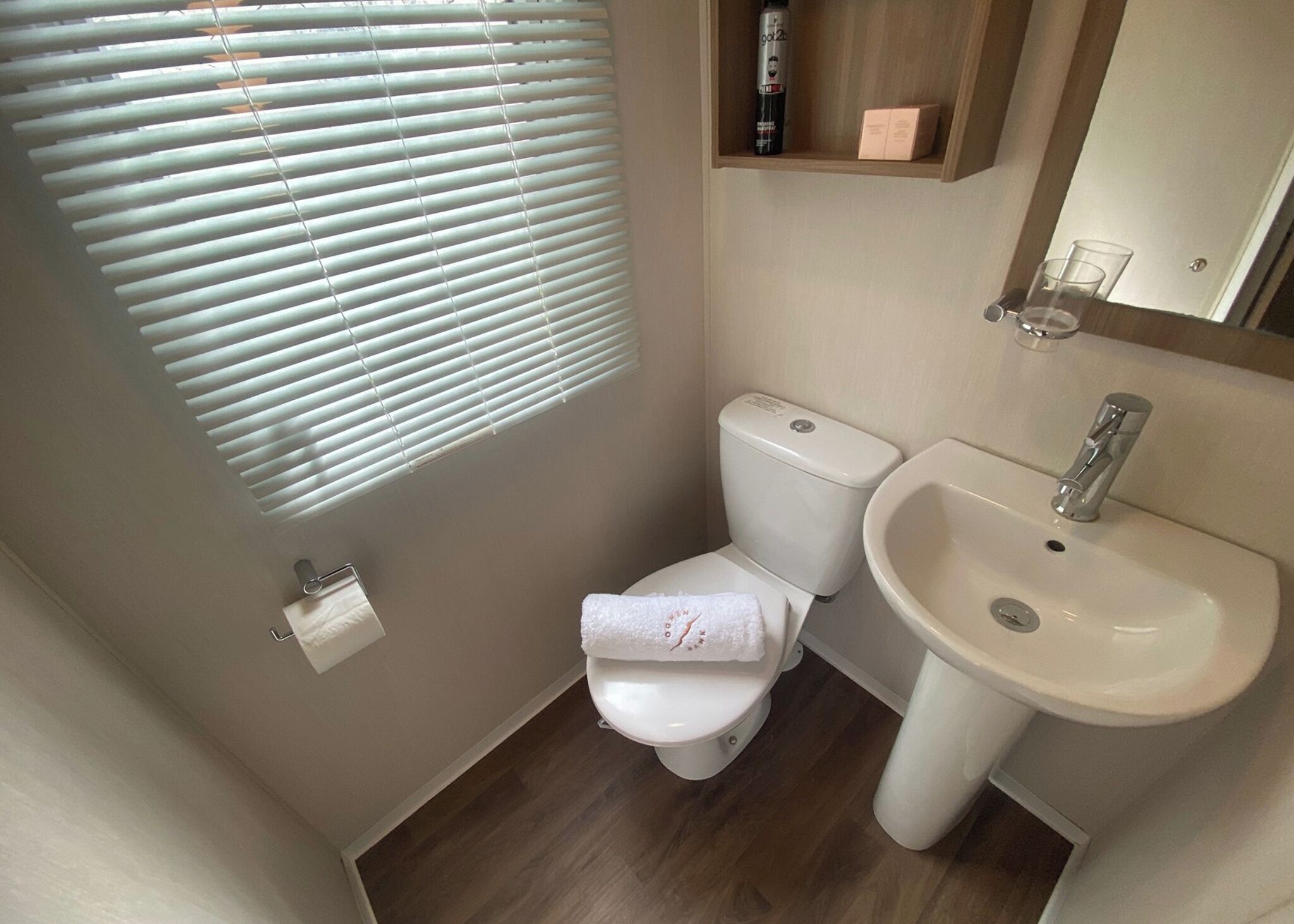 A compact bathroom with a toilet, sink, and window blinds.