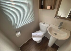 A compact bathroom with a toilet, sink, and window blinds.