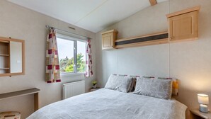 A bedroom with a bed, a window with curtains, a radiator, a bedside table with a lamp, and a wooden headboard.