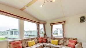 A cozy room with a sectional sofa, a small table, and large windows offering a view of mobile homes.