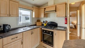 A compact kitchen with wooden cabinets, a Bosch oven, a window, and a fire extinguisher.