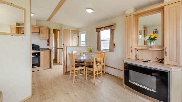 A compact kitchen with wooden cabinets, a dining table with chairs, a built-in oven, and a fireplace.