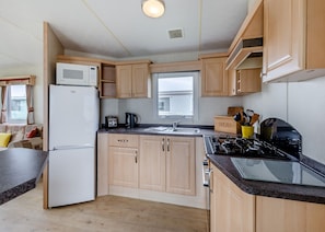 A compact kitchen with wooden cabinets, a built-in microwave, a gas stove, and a window providing natural light.