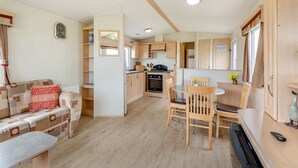 A compact kitchen with wooden cabinets, a dining area with a table and chairs, and a sofa with patterned cushions.