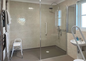 A bathroom with a glass-enclosed shower, a white sink, a mirror, and a white chair.