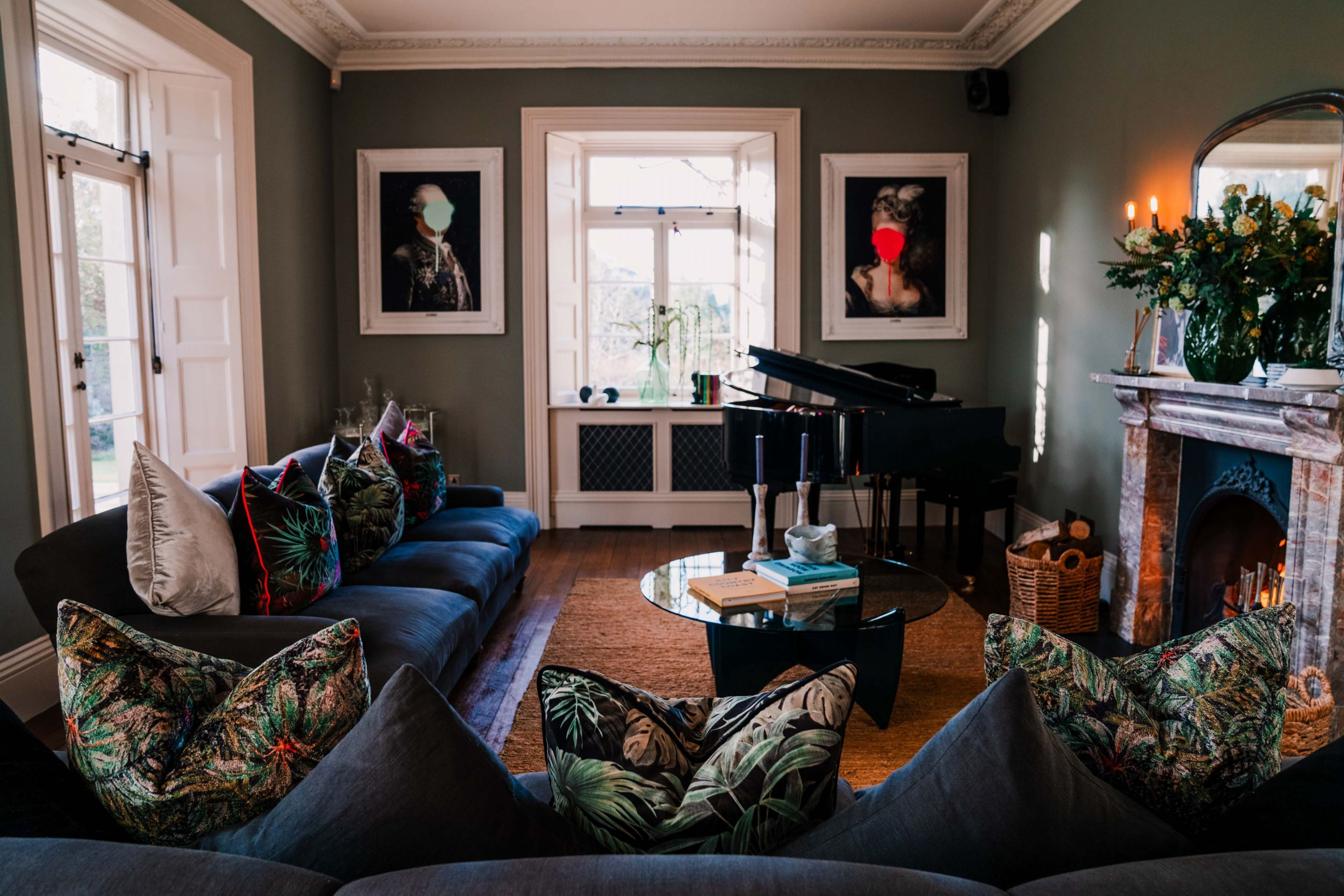 Sala de estar con sofá, mesa de centro y chimenea. Hay cuadros en la pared y un piano en la esquina.