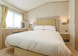 Ein Hotelzimmer mit einem großen Bett, Nachttischen, einem Spiegel und einem Fenster mit Vorhängen.