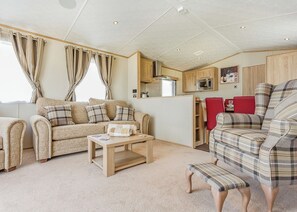 Ein gemütliches Wohnzimmer mit einer Couch, einem Couchtisch und einem roten Sessel. Es gibt eine Küchenzeile mit Holzschränken und einer Mikrowelle.